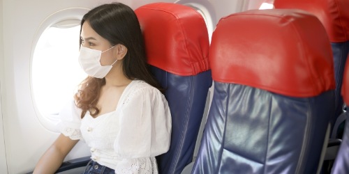 Touristin sitzt im Flugzeug mit Schutzmaske